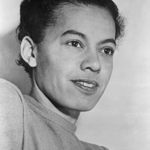 Pauli Murray is profiled to the left and is staring in the distance with a small smile on her face. She is wearing a shirt with a thin collar and her short hair brushed back.