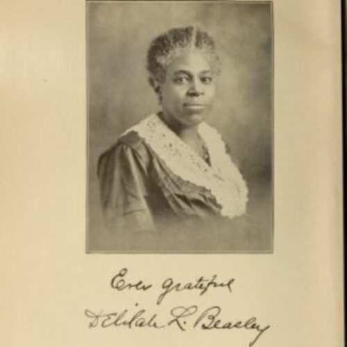 Delilah Beasley is seated in front of a portrait background. Her natural hair with streaks of grey is pulled back and she smiles without opening her mouth. She is wearing a dress with a ruffled lace collar. Beneath the photo is her signature that reads, “Enter grateful; Delilah R. Beasley.”