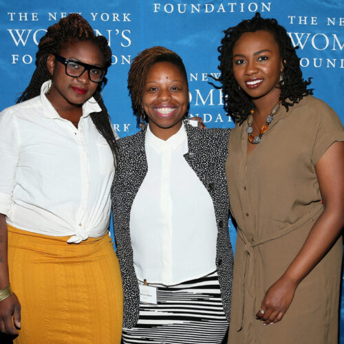 Colored photo of all three women standing together in front of a blue sign that reads "New York Women Foundation.