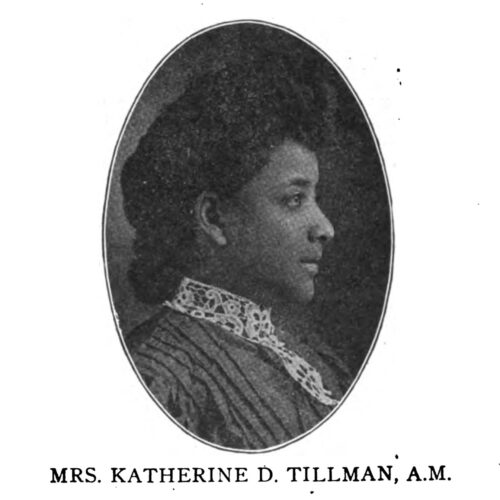 A side profile, bust portrait of Katherine Tillman. She wears a dark colored blouse with a lace color. Her natural hair is styled in an updo.