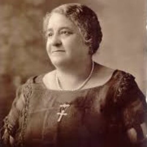 Maggie Lena Walker is looking toward the left with a slight smile, wearing pearls and a cross, short hair and a slightly scoop-necked dress. The photo is in tan sepia tones.