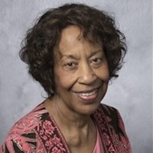 Beverly Shamana smiling, looking right, wearing a pink and black patterned top.