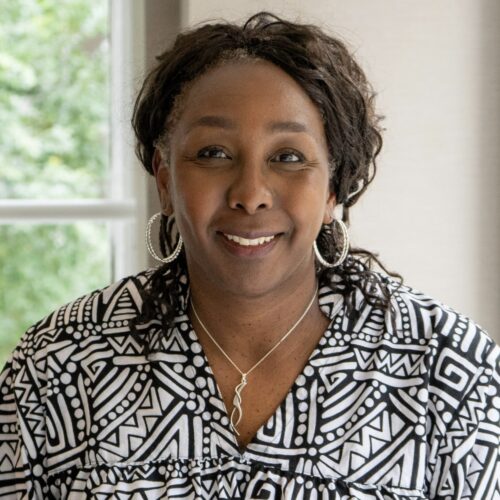 Vanessee Burns wearing a black and white shirt, with a necklace and earrings, hair pulled back, smiling.