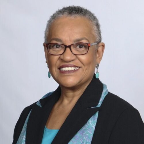 Darlene Garner, smiling, wearing glasses, turquoise earrings and turquoise scarf over black suit jacket with turquoise shirt underneath.