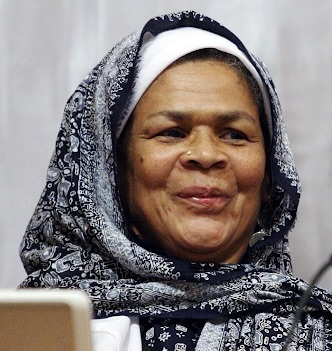 Amina Wadud, smiling, wearing a gray and black Hijab.
