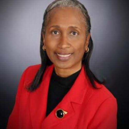 Cheryl Sanders, smiling, wearing a red jacket, a black shirt, a brooch and gold earrings.