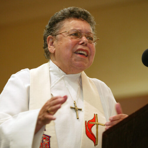 Leontine Kelly wearing a white clerical robe, with a cream colored stole, a cross, short hair, and glasses, preaching in front of a podium with her hands gesturing. United Methodist Bishop Leontine Kelly preaches during evening worship at the first reunion of the former Central Jurisdiction of the Methodist Church in College Park, Ga. The jurisdiction was a racially segregated structure for black Methodists that existed from 1939 to 1968, when it was dissolved into the five current geographic jurisdictions of the United Methodist Church.