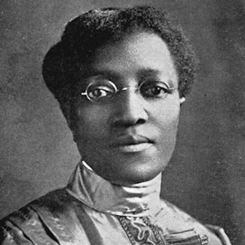 Clara Ann Howard wearing short hair, glasses, and a high-necked fancy top. The photo is in black and white.