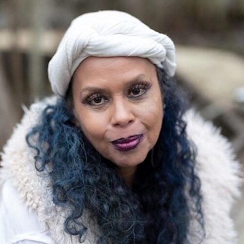 Lilith Dorsey wearing long curly hair, a white hat, and a white jacket with decorative furry lapel.