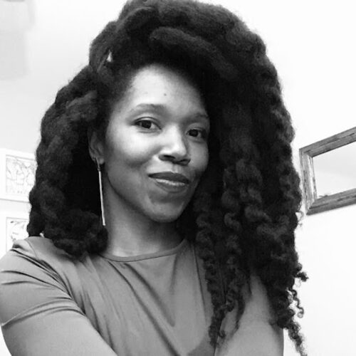 Amber Starks smiling with her curly hair parted and swept over on one side. The photo is in black and white.