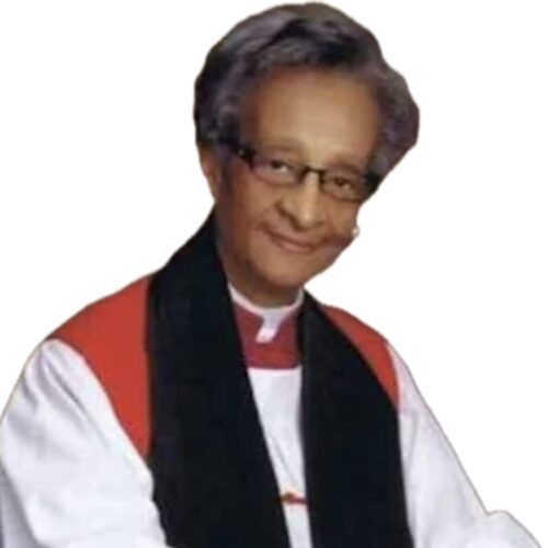 Audrey F. Bronson smiling, wearing a red and white clerical robe, a black stole, short gray hair, and glasses with her hands folded in front of her.