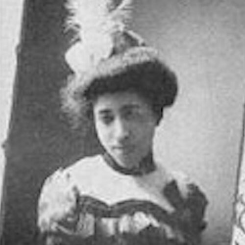 Alberta Moore-Smith, also known as Albreta, is wearing her hair up, with a fancy high-necked ruffled top, and a hat with a feather in it. The photo is in black and white.