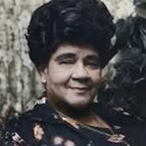 Arenia Mallory, smiling, wearing her up, and a V-necked black top with flowers and designs.