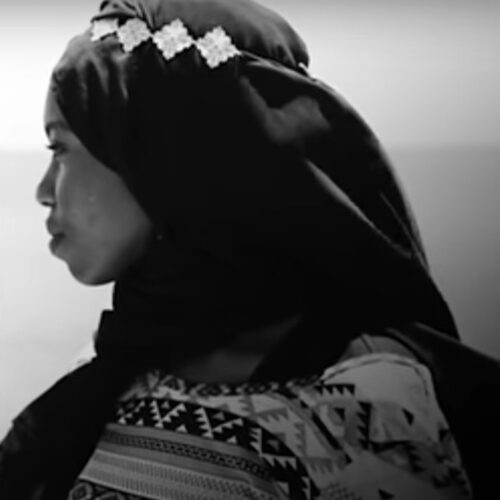 Emtithal Mahmoud facing her left, wearing a Shayla Hijab with diamond-shaped decorative band on it, and a patterned top. The photo is in black and white.