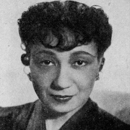 Etta Moten Barnett, wearing her hair short with wavy bangs, earrings, and a dark colored V-necked top. The photo is in black and white.