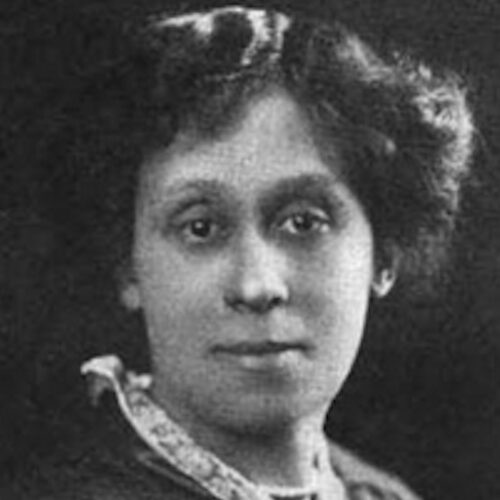 Eva del Bowles, wearing her hair short and parted on her left side, with a lace collared jacket over a top. The photo is in black and white.